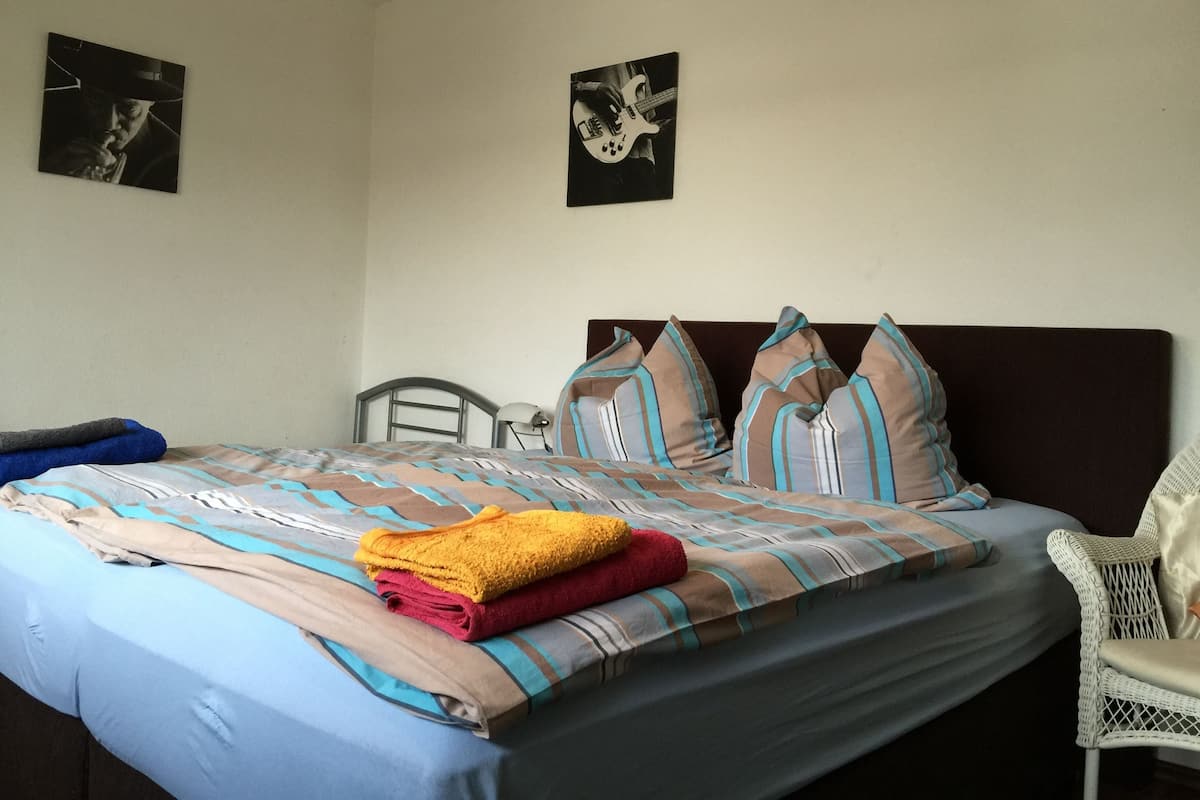 A neatly made bed with striped bedding, a chair, and two framed pictures on the wall.