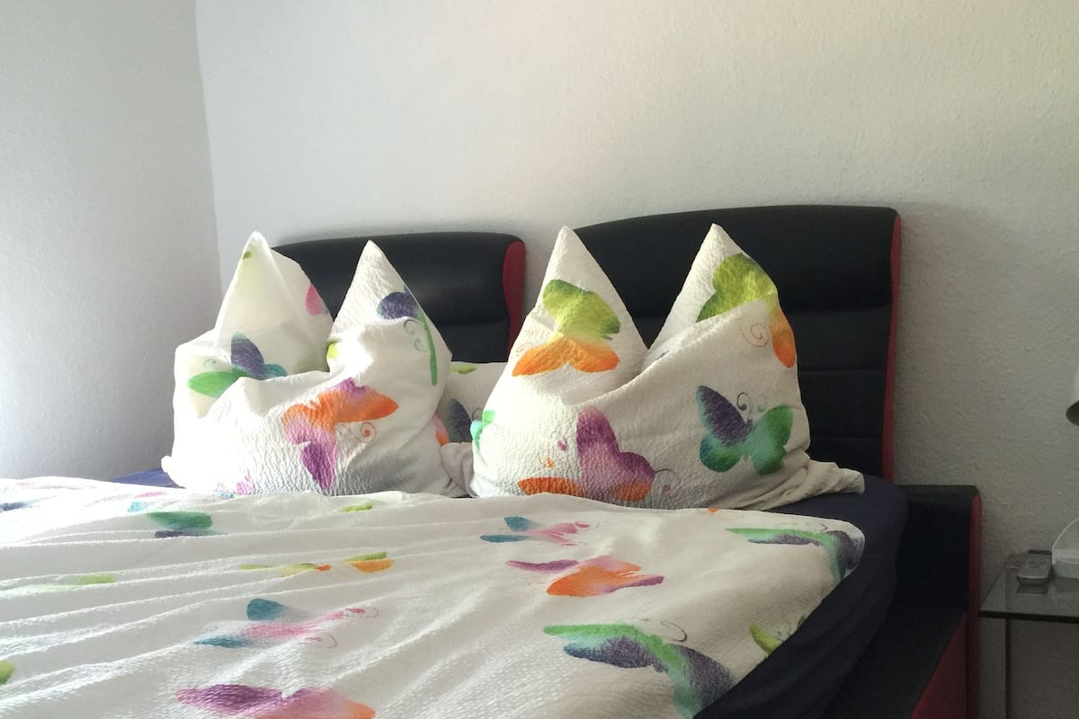 A bed with a white bedspread featuring colorful butterfly patterns, a black headboard, and two decorative pillows with butterfly designs.