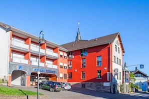 A hotel with a red facade, a parking area, and a church spire in the background.