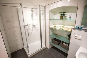 A modern bathroom with a glass-enclosed shower, a glass shelf with towels, and a white toilet.