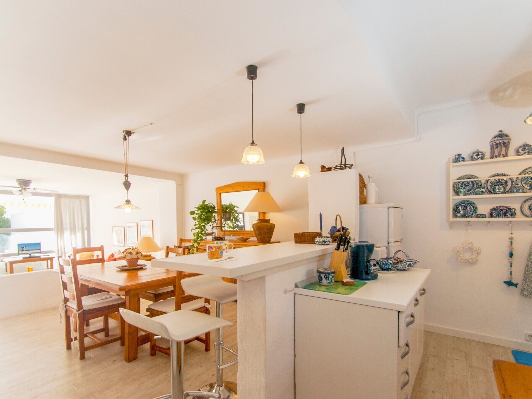 Una cocina moderna con una isla central, luces colgantes y un comedor con sillas y una mesa de madera.