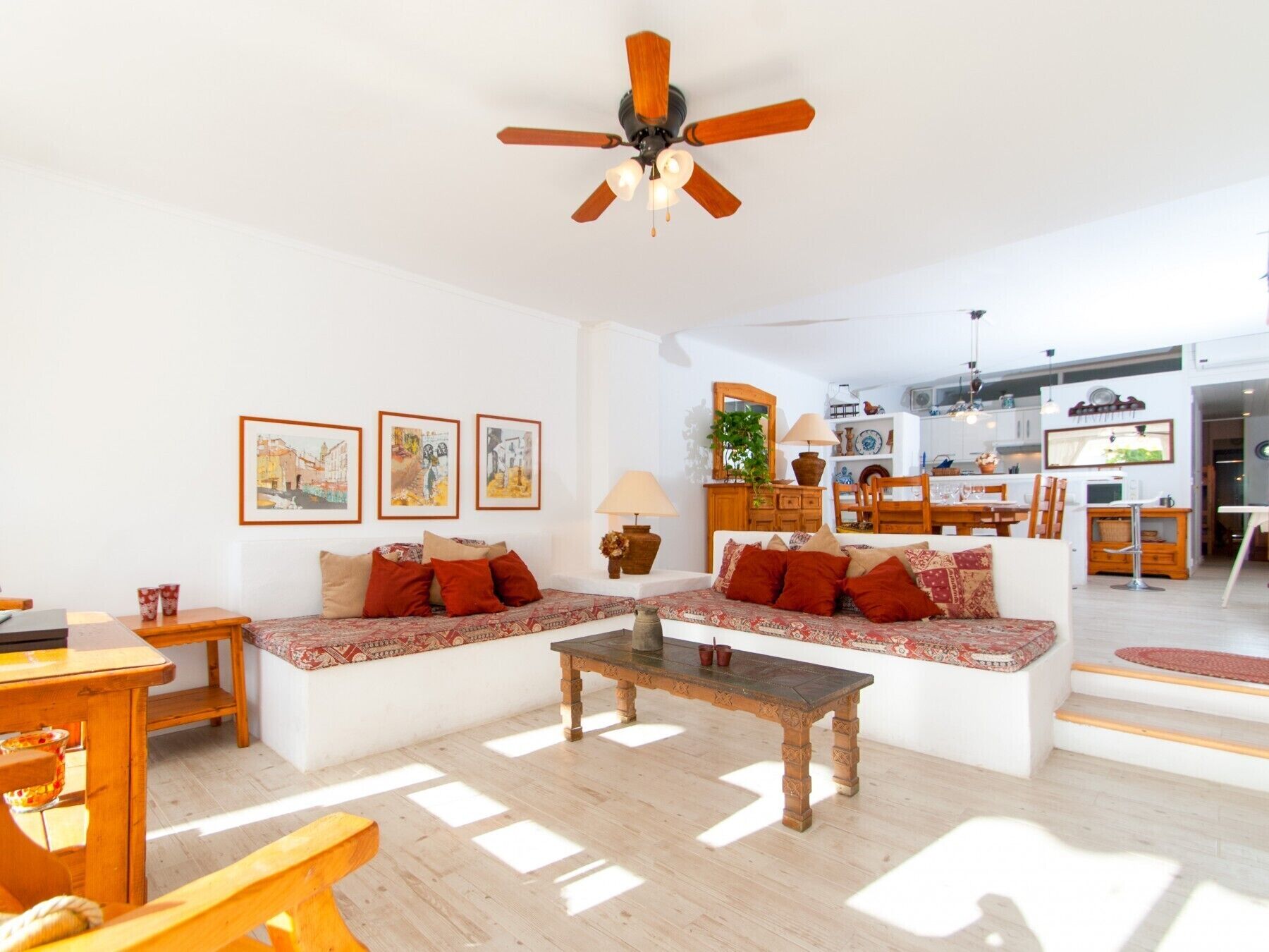 Ein großzügiges Wohnzimmer mit Couchtisch aus Holz, einer Couch mit gemusterten Kissen und einem Deckenventilator.