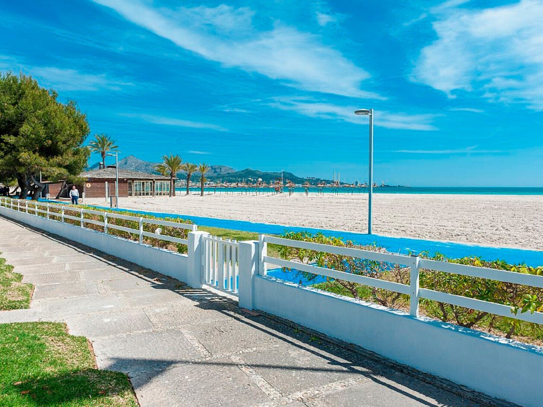 Une promenade en bord de mer avec une rambarde blanche, un ciel bleu dégagé et une plage en arrière-plan.