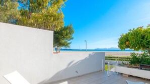 A terrace with white chairs and a table, overlooking a beach and the sea.
