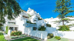 A modern white building with multiple balconies, a well-maintained lawn, and a tree.