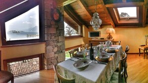 Comedor con pared de piedra, vigas de madera y vista al mar.