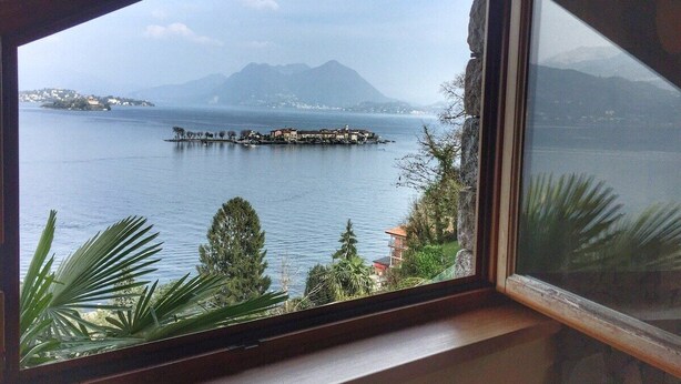 Vista desde una ventana sobre un cuerpo de agua tranquilo con una pequeña isla y montañas a lo lejos.