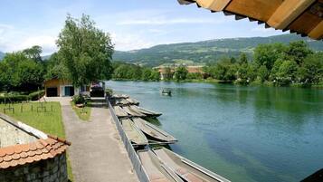 Un quai au bord de la rivière, avec des bateaux amarrés, un petit bâtiment et une vue sur un paysage verdoyant et vallonné.