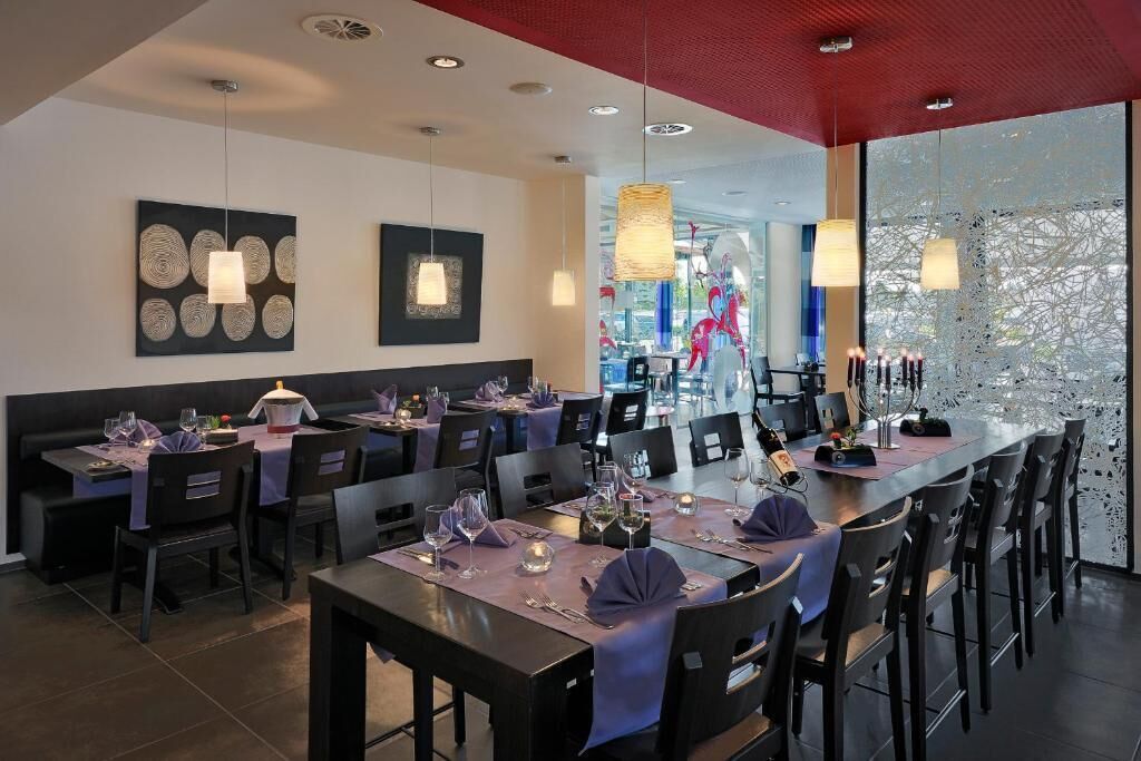 A modern restaurant with multiple dining tables, black chairs, and pendant lighting.