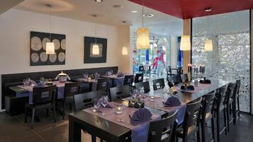 A modern restaurant with multiple dining tables, black chairs, and pendant lighting.