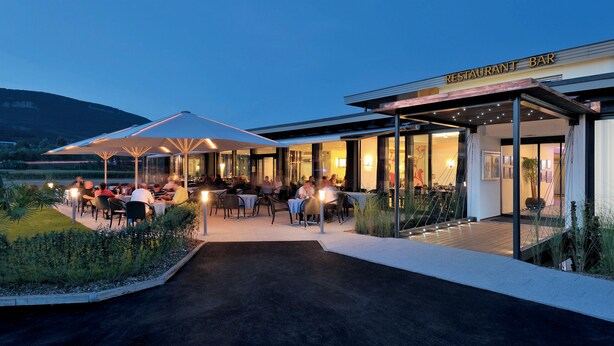 An outdoor restaurant bar with tables and umbrellas, surrounded by greenery and a view of the landscape. - Hotel Al Ponte (Wiedlisbach)