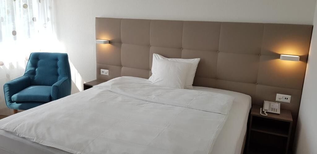 Ein Hotelzimmer mit einem großen Bett, einem blauen Sessel und zwei Nachttischlampen.