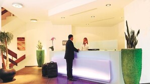 A reception area with a modern reception desk, a staircase, and potted plants. - Hotel Al Ponte (Wiedlisbach)
