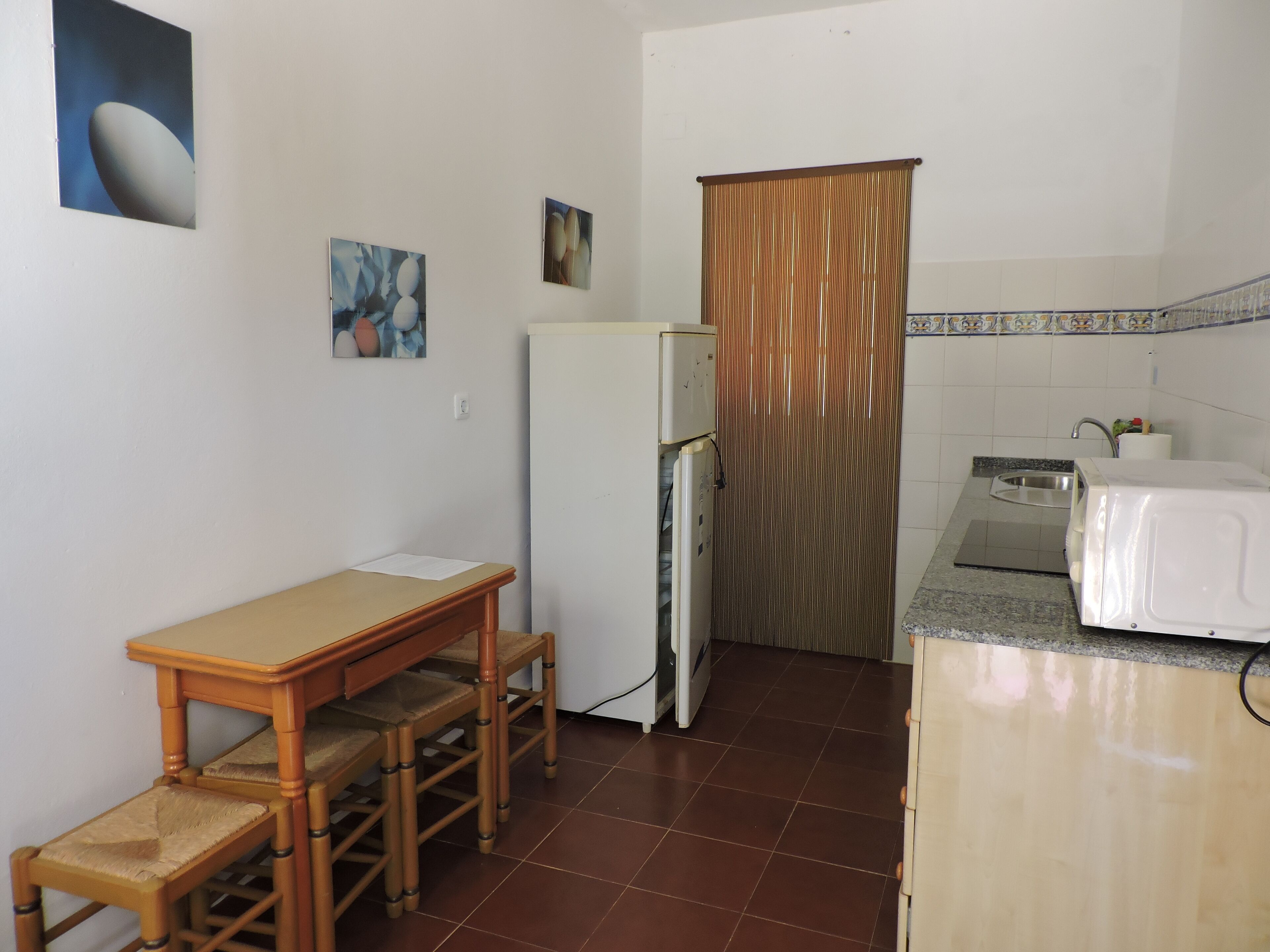 A compact kitchen with a wooden table and chairs, a refrigerator, a microwave, and a sink.