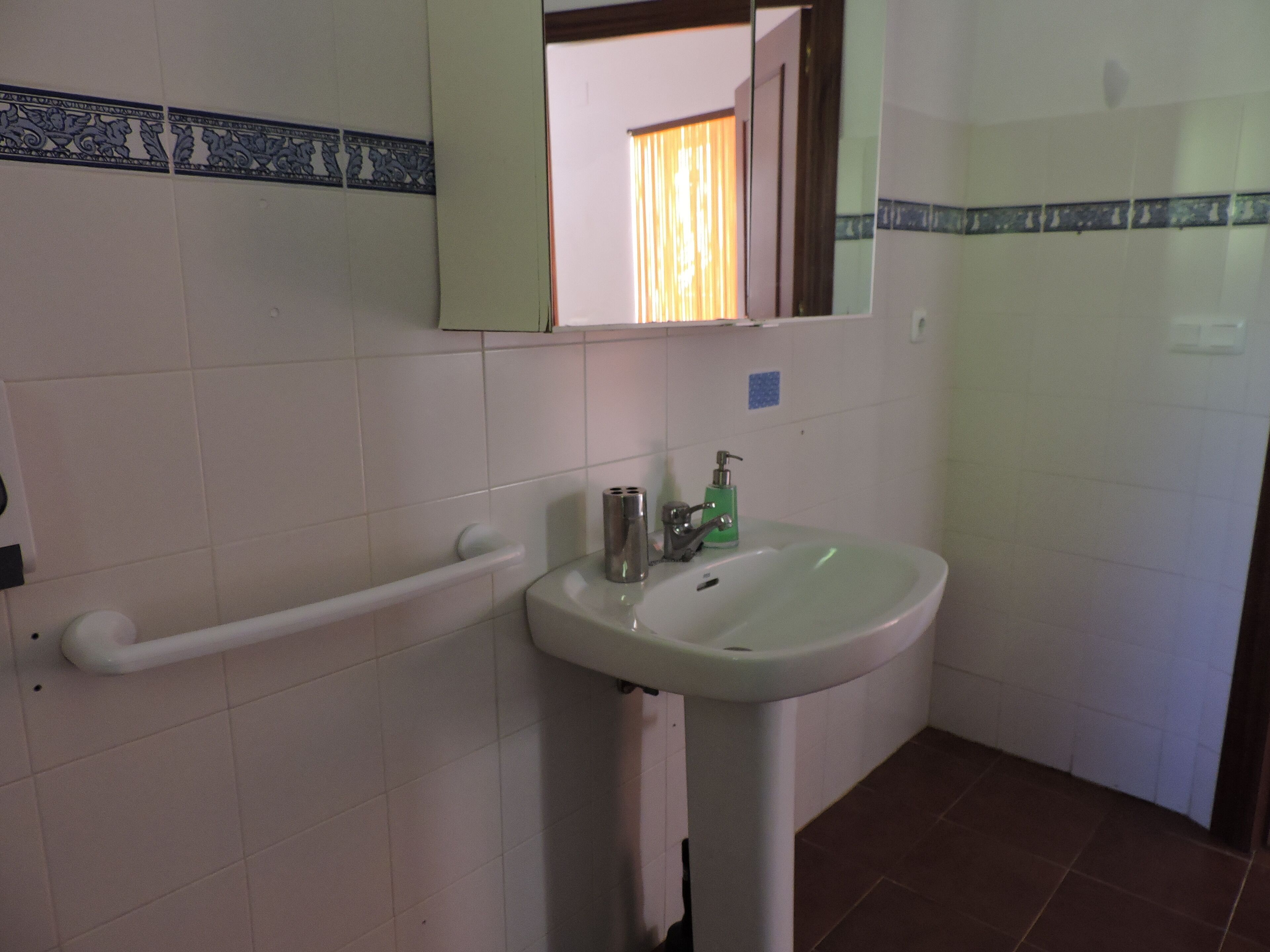 Un baño con lavamanos blanco, un espejo y una barandilla.