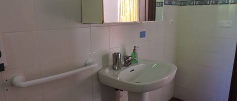 Un baño con lavamanos blanco, un espejo y una barandilla.