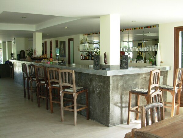 Une cuisine spacieuse dotée d’un grand îlot central, de chaises en bois et d’un coin bar avec des étagères remplies de bouteilles et de verres.
