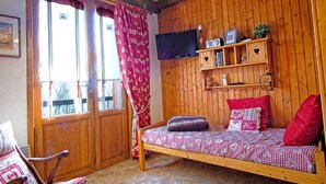 Una habitación acogedora con una cama de madera, un televisor montado en la pared y una ventana con cortinas.