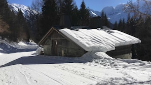Una cabaña de madera con techo inclinado, rodeada de nieve y árboles.