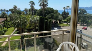 A balcony with a clear view of a parking area, palm trees, and a distant coastline.