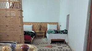 A room with a bed, a wooden headboard, a woven basket, a table with decorative items, and a patterned rug.