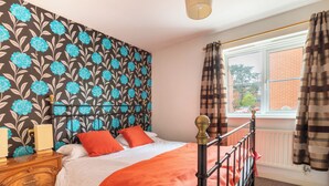 Quarto com cama, penteadeira, janela com cortinas e papel de parede estampado.