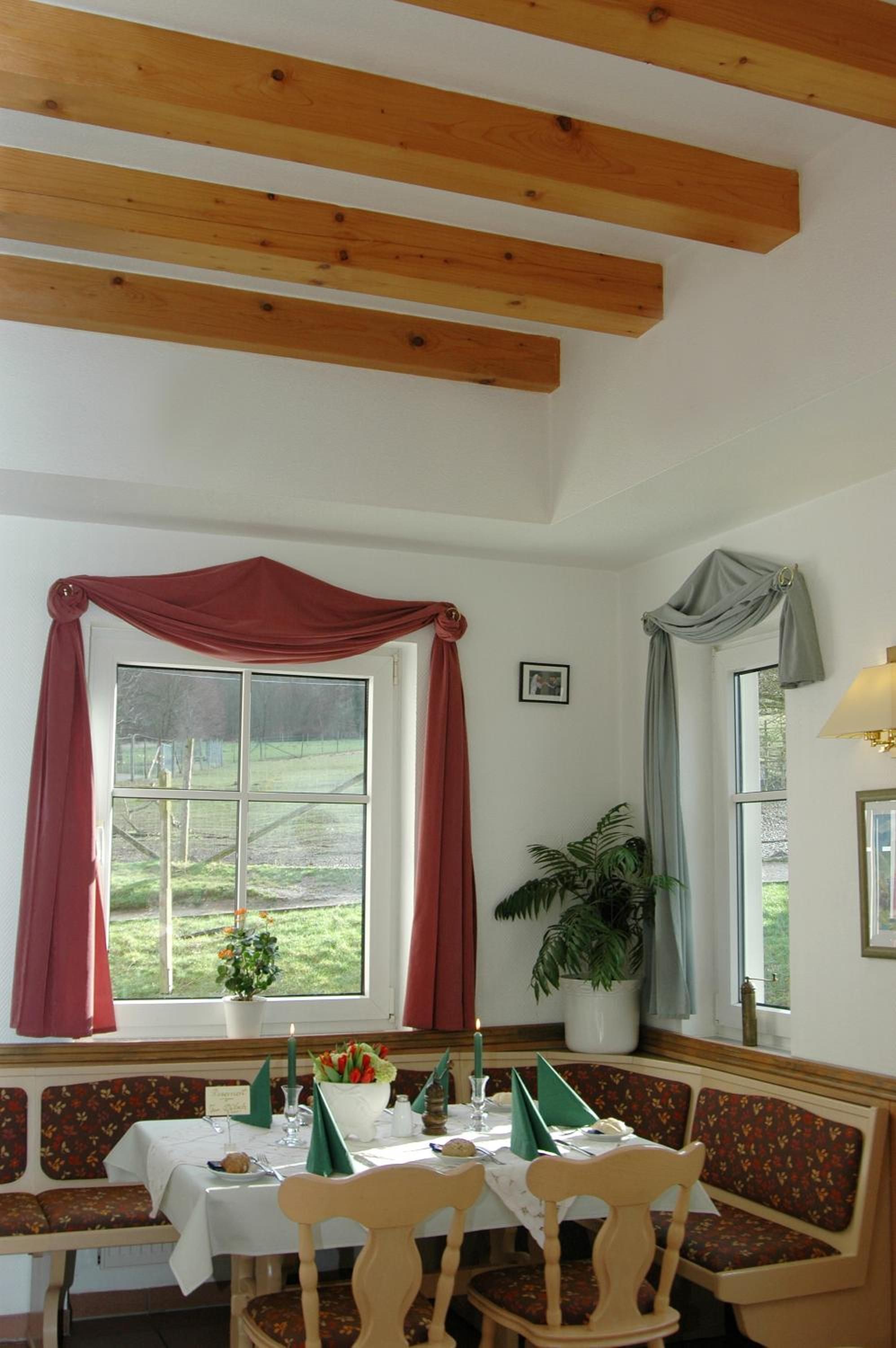 A dining area with a table set for two, a bench, and a window with curtains.