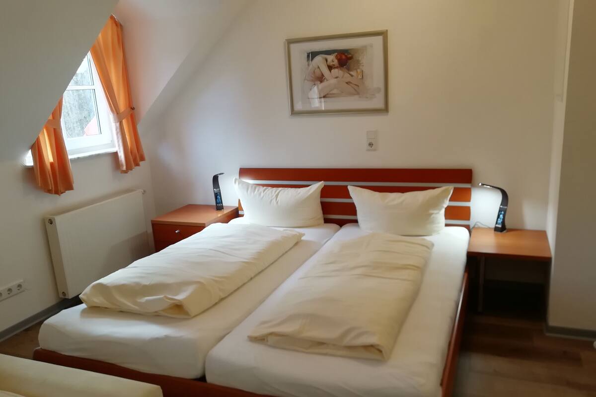 A hotel room with two beds, a painting on the wall, and a window with curtains.