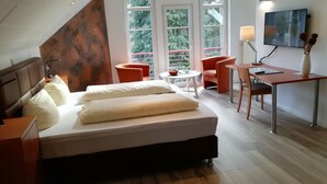 A modern bedroom with a large bed, a desk, two chairs, and a TV. - Waldhotel Forsthaus Remstecken (Koblenz)