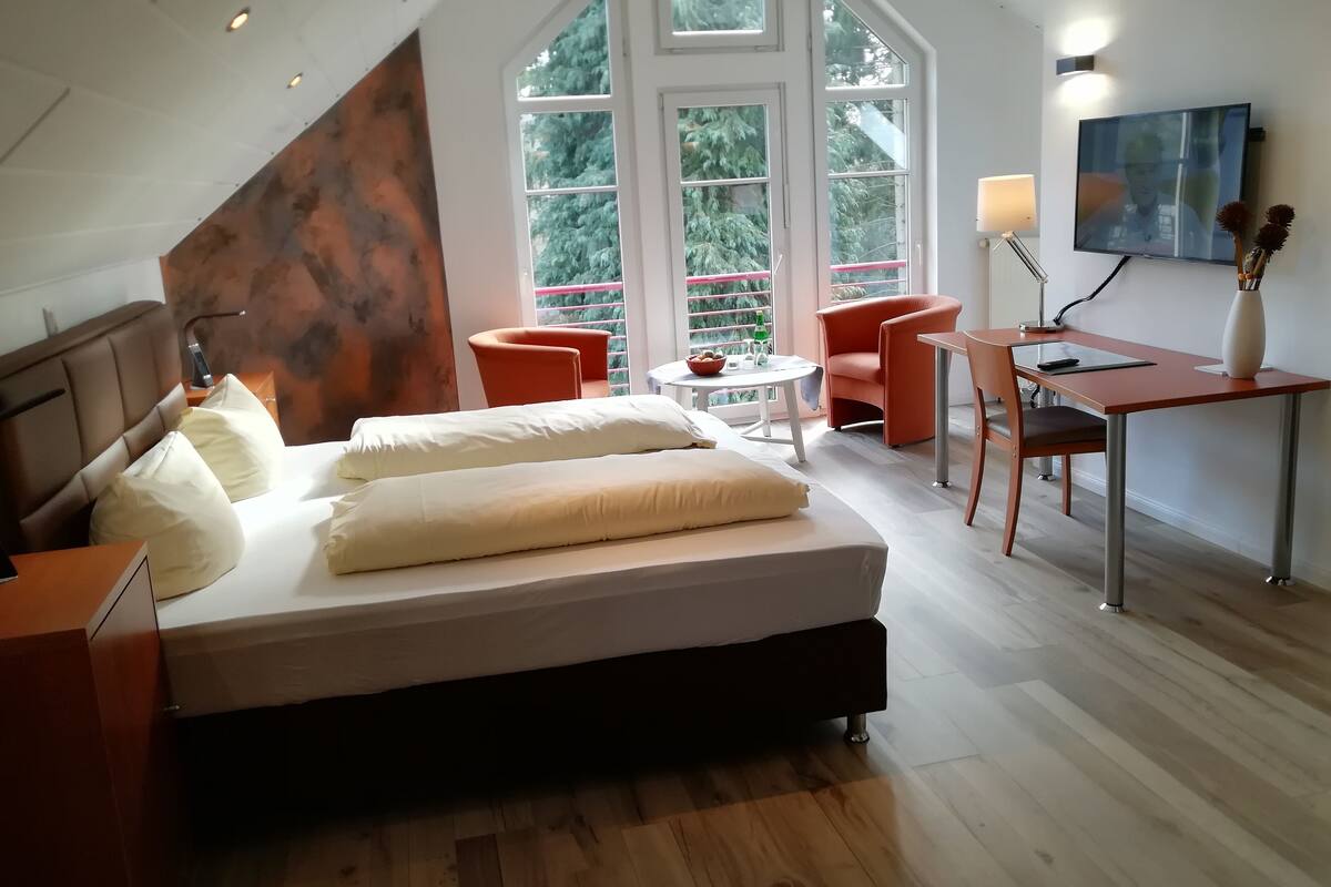 A modern bedroom with a large bed, a desk, two chairs, and a TV.