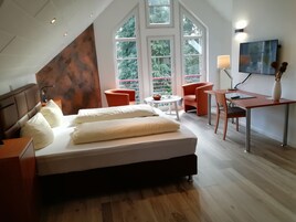Un dormitorio moderno con una cama grande, un escritorio, dos sillas y un televisor.