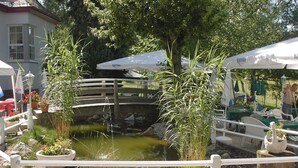 A garden area with a pond, a wooden bridge, and outdoor seating under umbrellas. - Waldhotel Forsthaus Remstecken (Koblenz)