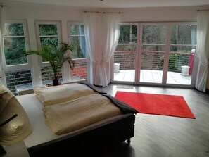 A bedroom with a bed, a red rug, a potted plant, and a view of a balcony with a railing. - Waldhotel Forsthaus Remstecken (Koblenz)