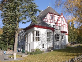Una casa tradicional con entramado de madera, base de piedra, ventanas grandes y techo rojo.