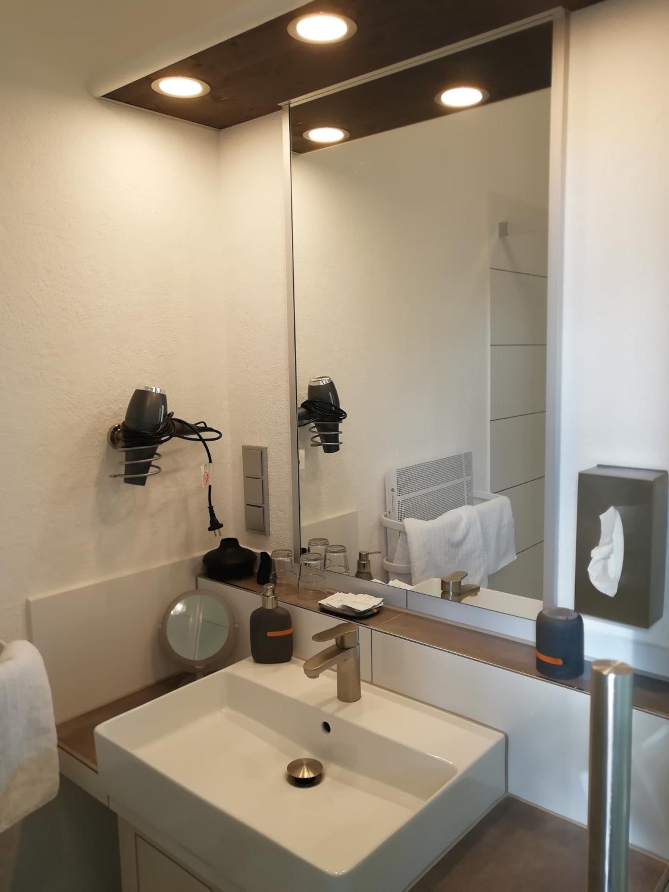 Un baño moderno con un espejo grande, un lavamanos y dos secadores de pelo fijados en la pared.
