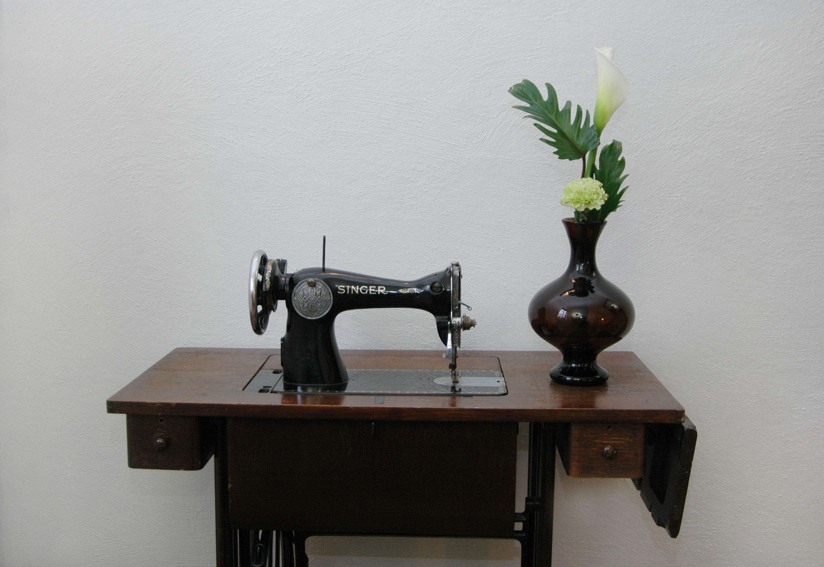 Una máquina de coser Singer sobre una mesa de madera con un florero de flores.