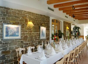 A long dining table set for a meal with white tablecloths and napkins, wooden chairs, and framed artwork on the stone wall. - Waldhotel Forsthaus Remstecken (Koblenz)