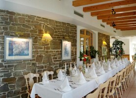 Una larga mesa de comedor preparada para una comida, con manteles y servilletas blancos, sillas de madera y cuadros en la pared de piedra.