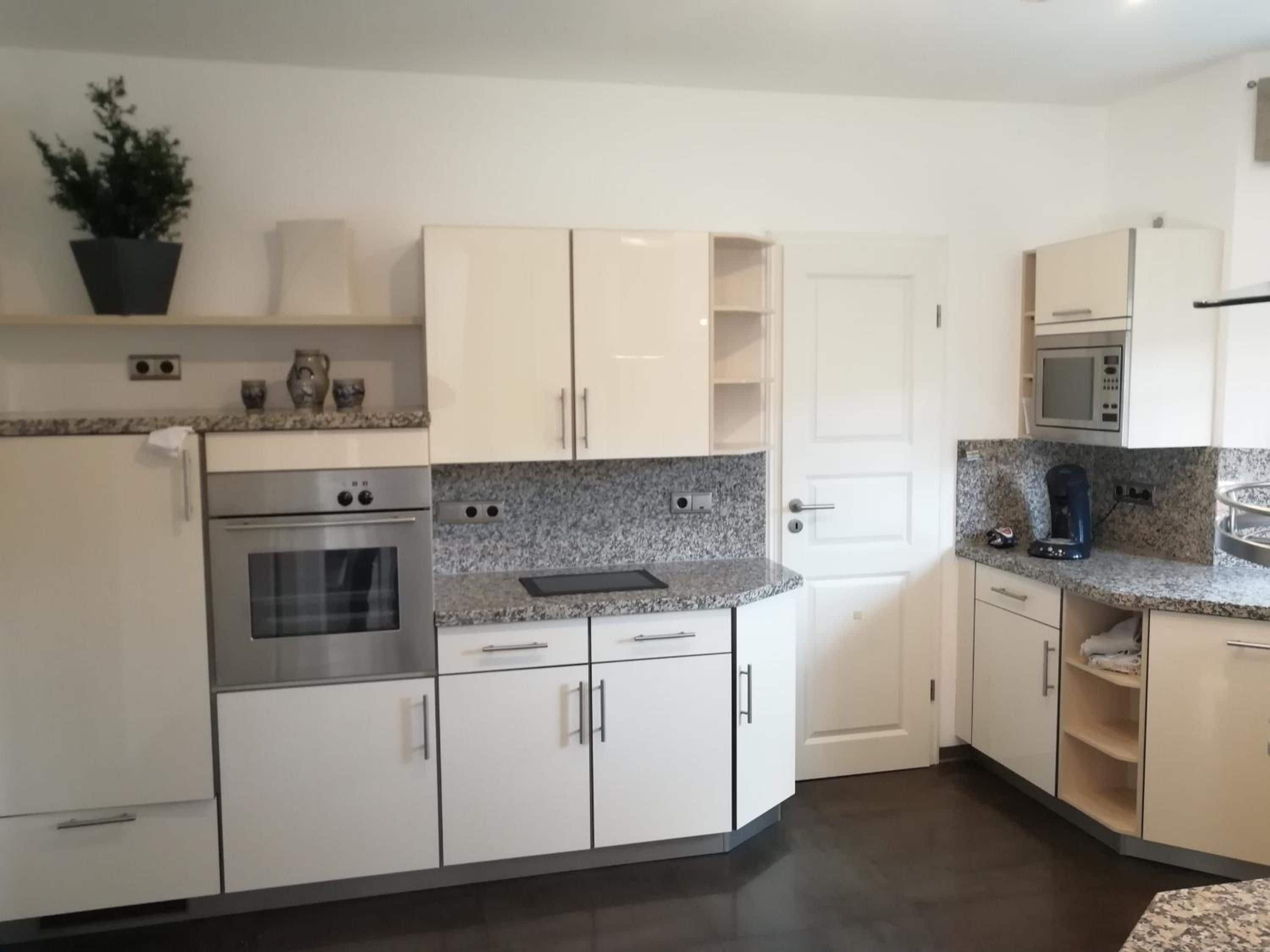 Una cocina moderna con gabinetes blancos, encimeras de granito, horno integrado y microondas.
