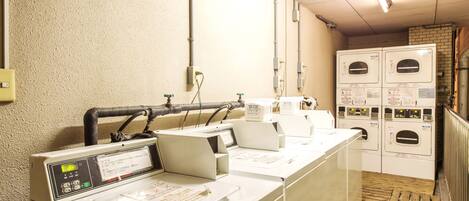 A laundry area with multiple washing machines and dryers, a control panel, and a wooden floor.