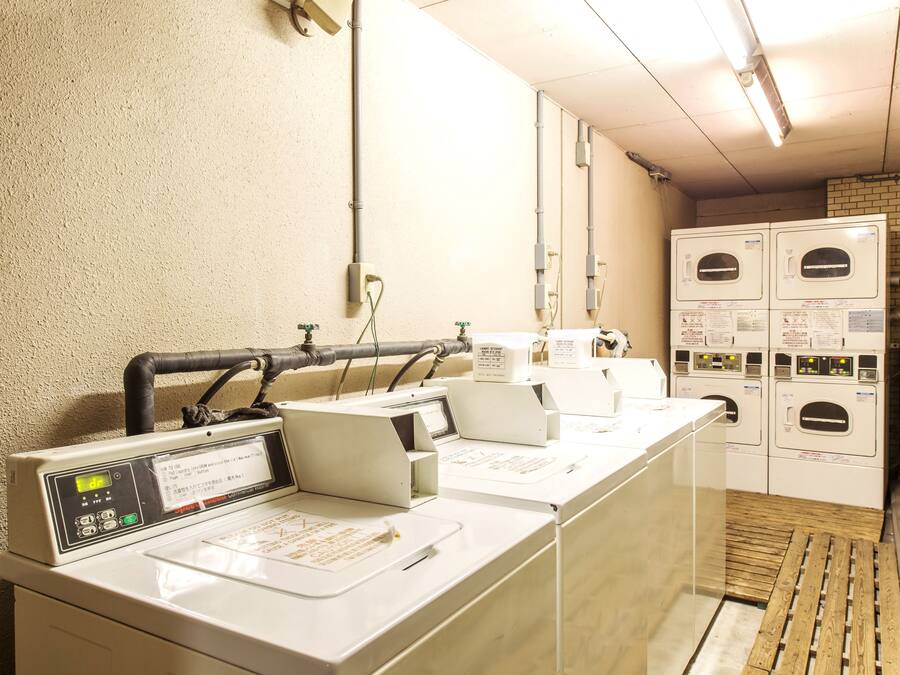 A laundry area with multiple washing machines and dryers, a control panel, and a wooden floor.