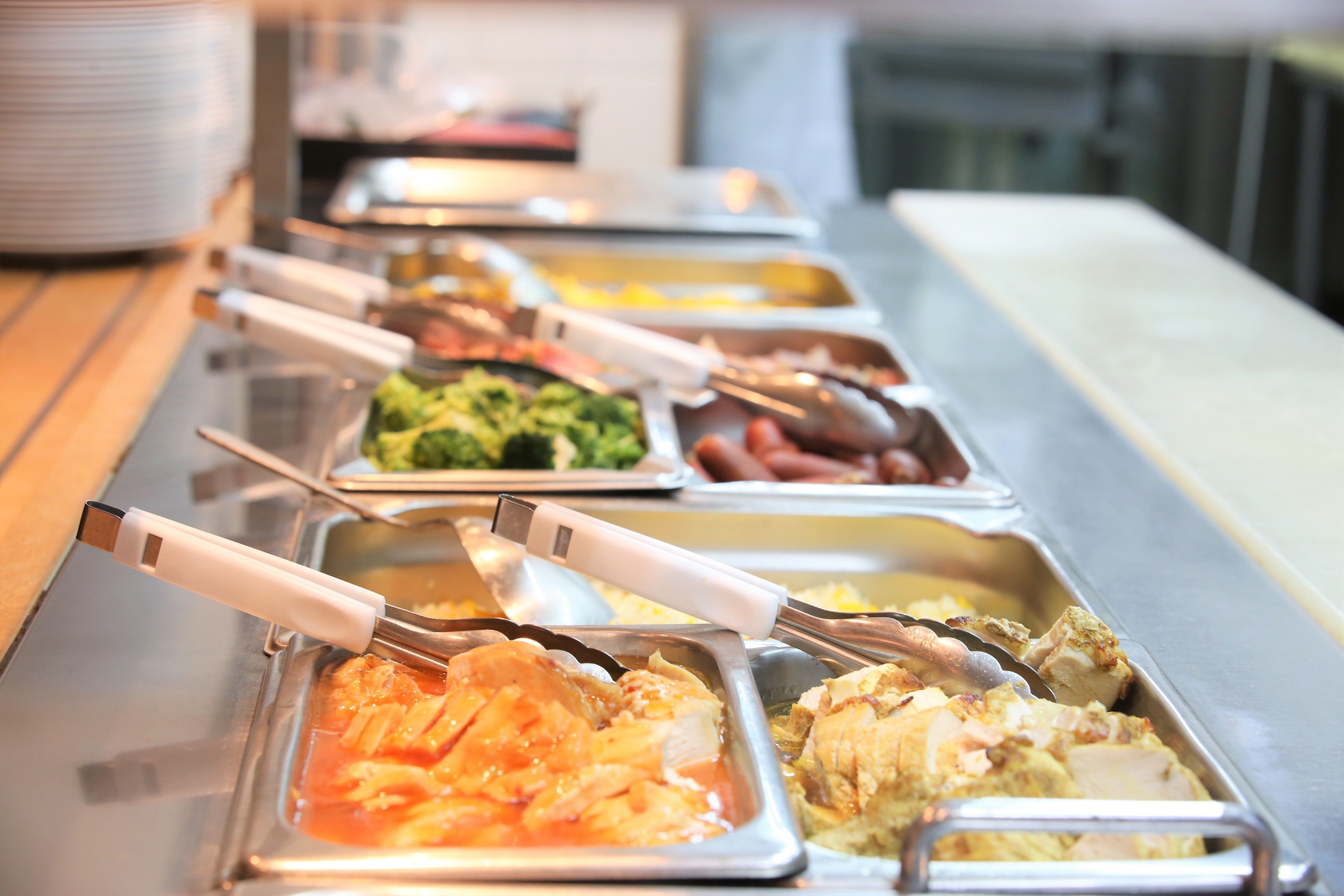 A buffet line with various food options, including pasta, chicken, and vegetables.