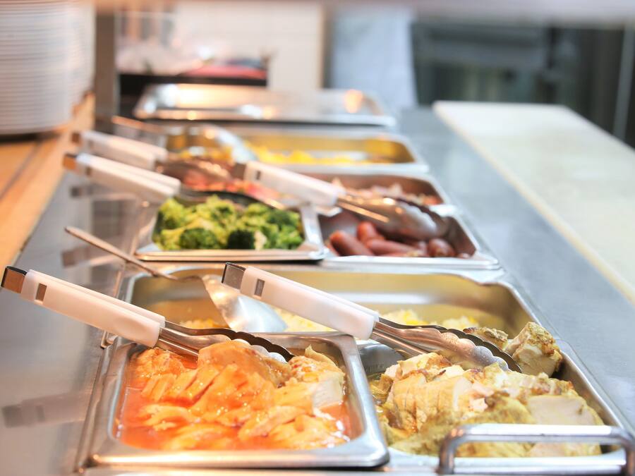 Una barra de buffet con diversas opciones de comida, como pasta, pollo y verduras.