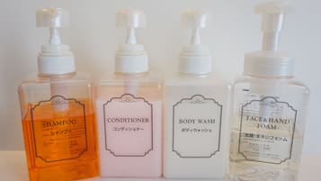 Cuatro botellas de productos de cuidado personal: champú, acondicionador, gel de baño y espuma limpiadora facial y para manos.