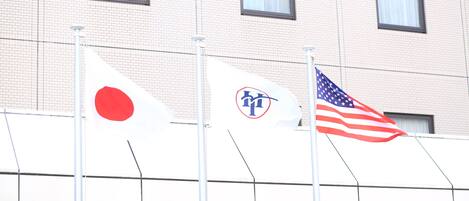 Three flags on flagpoles in front of a building with a tiled facade and windows.
