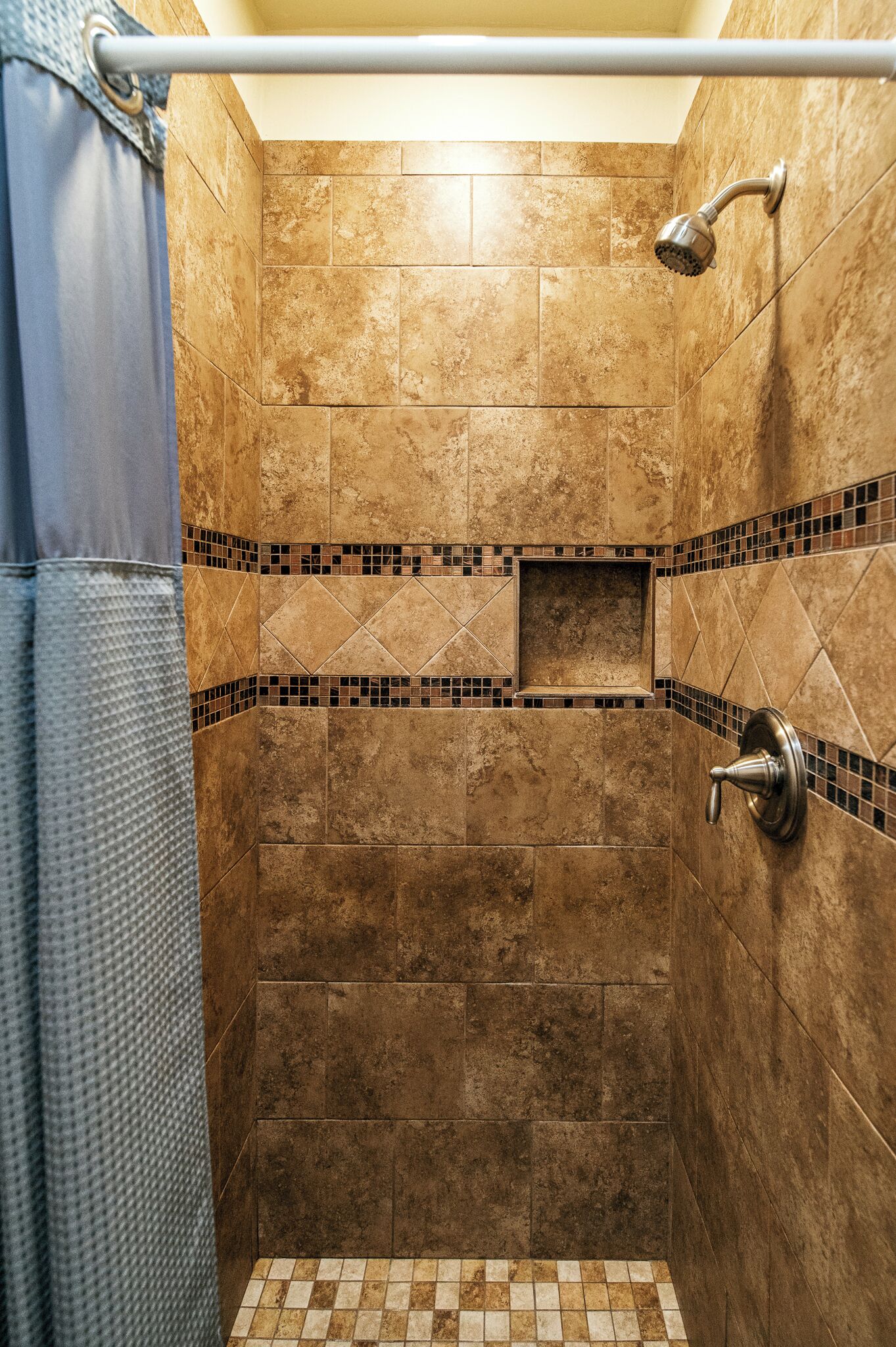 Une douche avec un pommeau de douche amovible, un porte-serviettes et une petite étagère dans le coin.