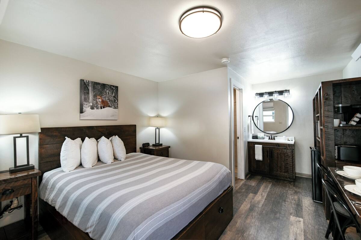 A bedroom with a bed, bedside lamps, a nightstand, a mirror, a sink, and a wooden cabinet.