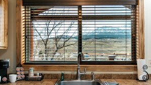 Una cocina con un lavamanos de acero inoxidable, una cafetera y una ventana con persianas.