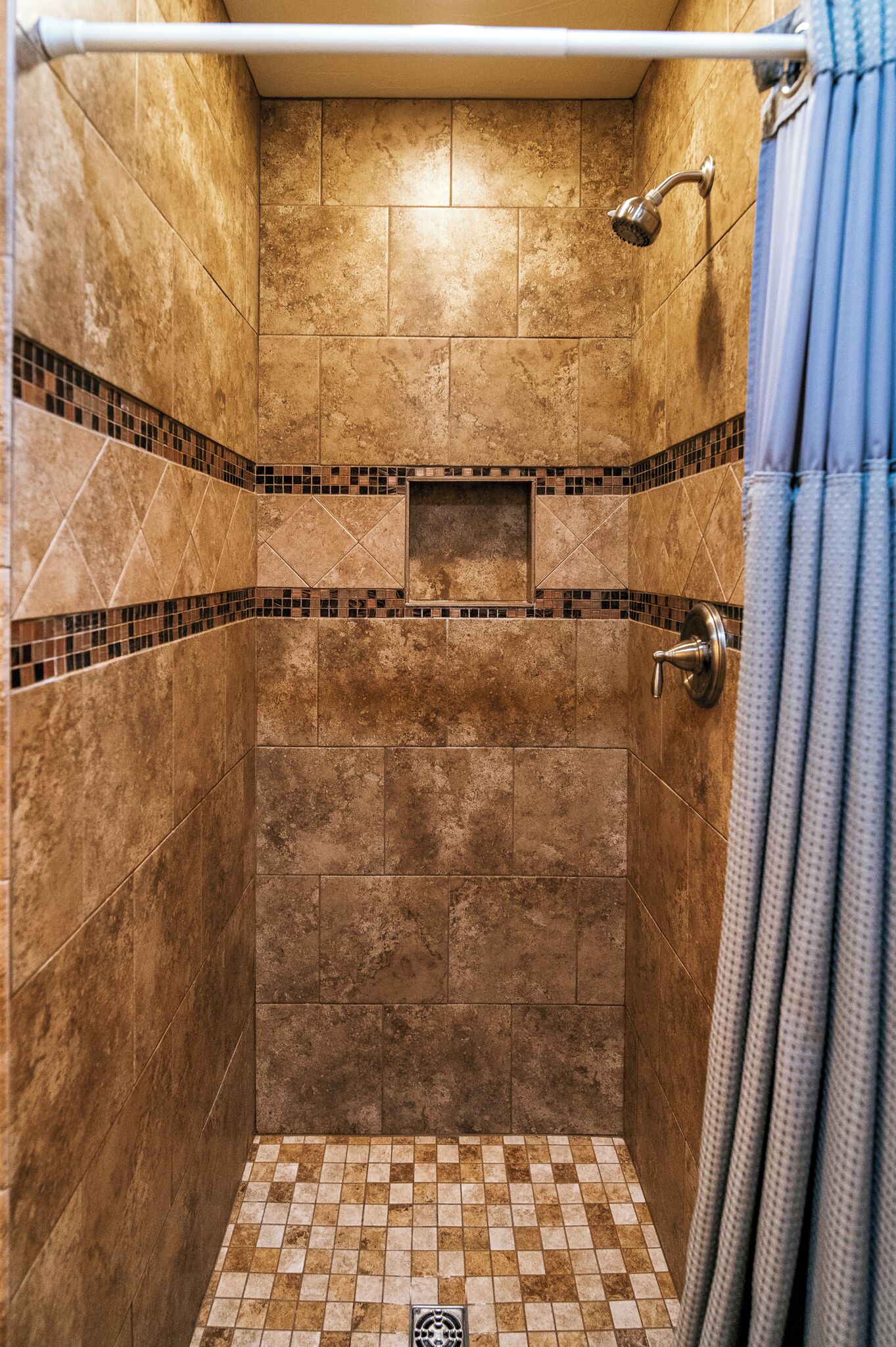 A shower with a tiled floor and walls, a showerhead, and a curtain rod.