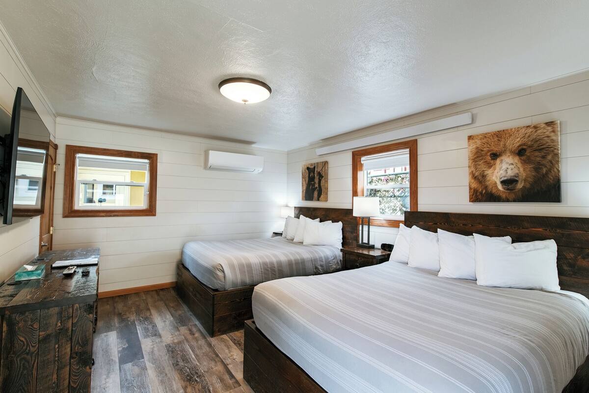 A bedroom with two beds, a wooden dresser, a mirror, and a bear painting on the wall.